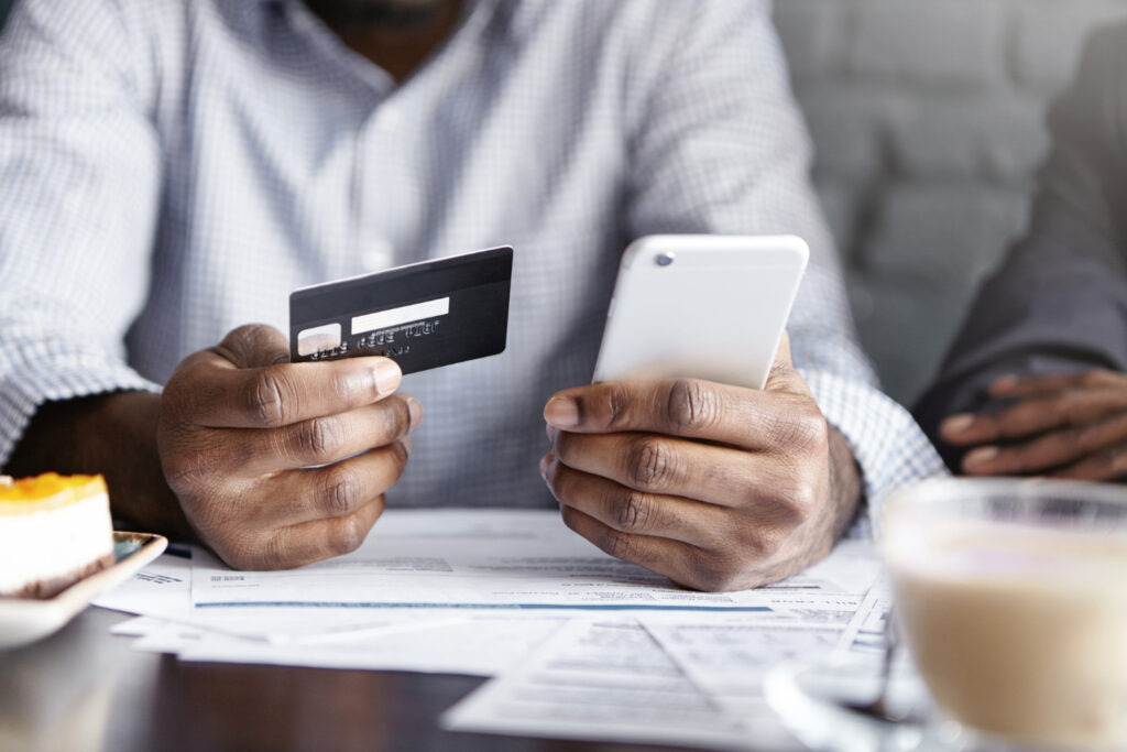 Un homme tenant une carte bancaire et un smartphone effectuant un paiement en ligne.