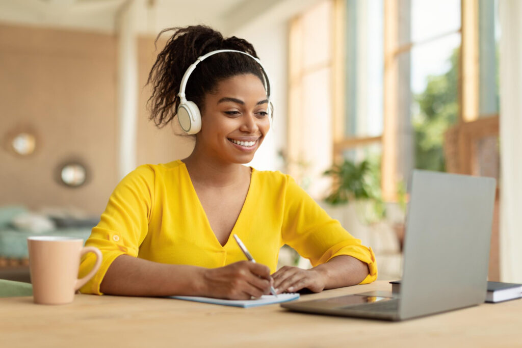 Une jeune femme avec un casque sur la tête en train de prendre des notes, assistant à une formation en ligne
